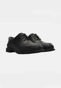 Black rubber shoes with a rounded toe, lace-up design, and textured sole. Features a thick sole with vertical grooves for traction.