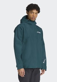 Teal wodoodporny kurtka z kapturem, z zamkiem błyskawicznym z przodu i regulowanymi mankietami. Wyraźne logo Gore-Tex i Terrex na klatce piersiowej i rękawie.