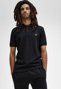 Polo nero con tessuto testurizzato, dotato di una pattina con due bottoni, maniche corte e un logo giallo sul lato sinistro del petto.