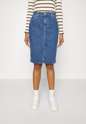 Vrouw draagt een blauwe denim rok tot op de knieën met een voorste split, een gestreept shirt met lange mouwen, witte sokken en witte sneakers.