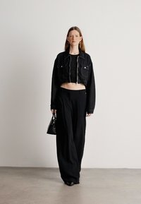 Crna skraćena traper jakna preko crnog kratkog topa, uparenih s ležernim crnim hlačama. Model nosi malu crnu torbicu i crne cipele.