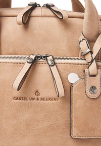 Tan leren tas met een gestructureerd oppervlak, twee ritscompartimenten, bijpassende tabaccenten en een klein bevestigd label. Bevat een geperst logo.