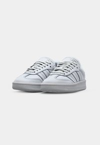 Weiße Sneakers mit einem glatten Obermaterial aus Leder, grauer Gummisohle und sechs Ösen. Verfügt über drei parallele Streifen auf jeder Seite und eine strukturierte Zehenkappe.