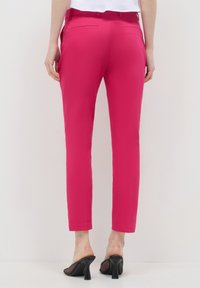 Knallpinke, taillierte Hose mit Slim Fit, versehen mit Gesäßtaschen und einer glatten Textur. Kombiniert mit schwarzen Sandalen mit offenem Zehenbereich.