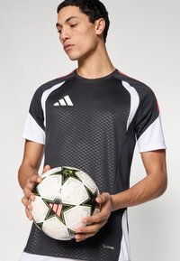 Μαύρο και άσπρο αθλητικό μπλουζάκι με τεχνολογία ClimaCool, με κόκκινες λεπτομέρειες και γεωμετρικό μοτίβο. Ο παίκτης κρατάει μια ποδοσφαιρική μπάλα με σχέδιο αστεριών.