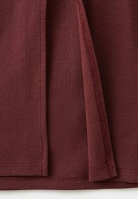 Gros plan sur un tissu bordeaux montrant un ourlet plié et des coutures détaillées le long du bord.