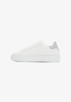 Zapatilla blanca de cuero con un acento plateado texturizado en el talón, cordones planos y una suela blanca gruesa. Diseño minimalista, textura suave.