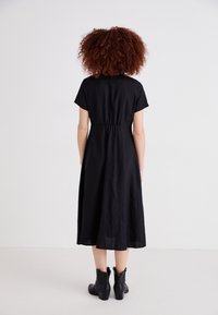 Rochie neagră, de lungime medie, cu mâneci scurte, talie elastică și fustă fluidă. Purtați cu cizme negre până la glezne. Material texturat.
