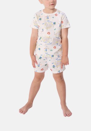 Dijete stoji boso, nosi bijelu majicu kratkih rukava i kratke hlače s šarenim uzorcima broda, drveta, srca i valova.