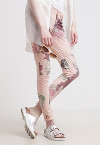 Roze legging met bloemenpatroon gemaakt van rekbare stof, gecombineerd met een losse witte blouse en metalen sandalen met twee gespen.