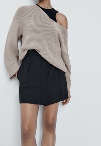 Beige ylipitkä neulepusero, jossa on kuvioitua tekstuuria, yhdistettynä mustaan, taitettuun mini-hameeseen, jossa on siisti ja räätälöity muotoilu.