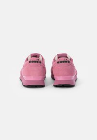 Diadora sneakers in light pink suede with rubber soles, featuring textured accents, rounded shape, and branding on the heel in black.