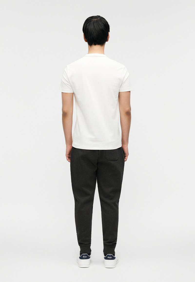 T-shirt en coton blanc pour homme et pantalon de survêtement gris foncé. Le t-shirt a des manches courtes, tandis que le pantalon de survêtement présente une coupe fuselée et des poches latérales.
