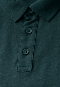 Mörkgrön polo-shirt med en texturerad tyg, treknapplista med mörka knappar och en klassisk kragdesign.