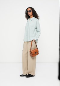 Light blue collared shirt with textured polka dots, beige wide-leg pants, black shoes, and a small brown crossbody bag. Sunglasses worn.