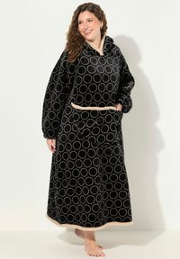 Robe di pile nera con un ampio motivo a cerchi beige, maniche lunghe, cappuccio e tasca frontale, con un bordo beige lungo l'orlo e in vita.