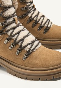 Barna velúr túracipő, puha fleece gallérral, sötét fűzőkkel, fémből készült fűzőlyukakkal és mély barázdákkal rendelkező masszív gumitalppal.