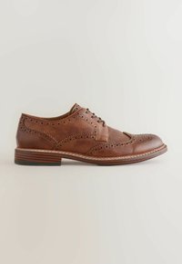 Chaussure brogue en cuir marron avec design à bout golf, détails perforés, talon empilé et fermeture à lacets sur un fond neutre.