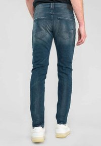 Blauwe denim jeans met een slim fit, voorzien van achterzakken, subtiele vervaging en stikseldetails. Gecombineerd met witte sneakers.
