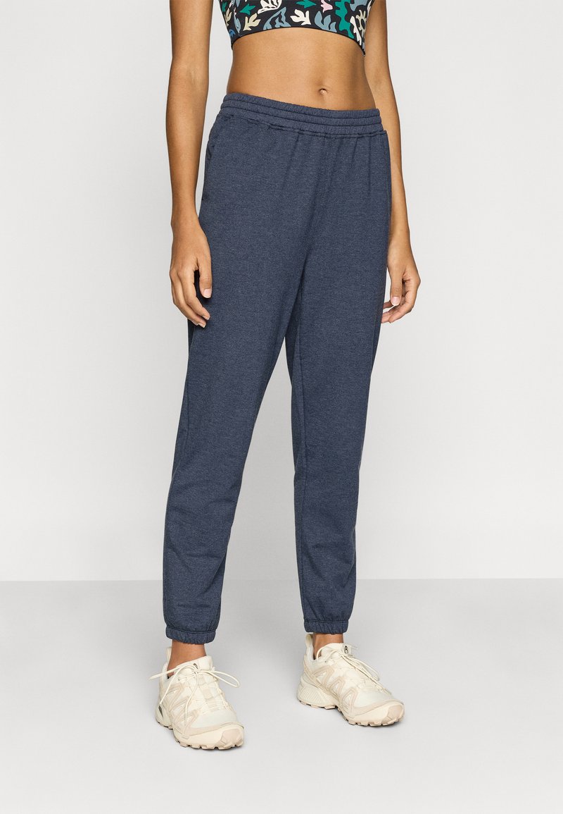 Σκούρο μπλε παντελόνι τζόγερ από μαλακό ύφασμα, με ελαστική μέση και κωνικά μπατζάκια. Συνδυασμένο με αθλητικά παπούτσια σε ουδέτερο χρώμα.