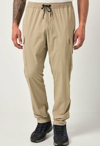 Pantaloni cargo leggeri beige con vita elastica e cordino, dotati di tasche laterali e polsini affusolati, abbinati a scarpe nere.