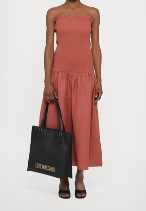 Zwarte totebag met "LOVE MOSCHINO" in gouden letters, gecombineerd met een roestkleurige, strapless, gerimpelde jurk met een gerimpeld lijfje.