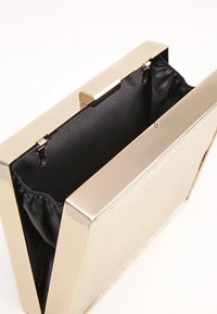 Metallinen kultainen kukkaro, jossa on teksturoitu pinta. Varustettu mustalla samettisella sisäpuolella, jossa on poimutettu avaaminen ja kultainen suljenta.