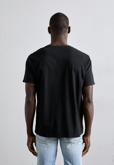 Musta puuvillainen t-paita lyhyillä hihoilla, pyöreä kaulus ja rento malli, jota on yhdistetty vaaleansinisiin farkkuihin. Ei näkyviä kuvioita tai korostuksia.