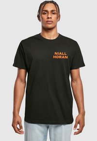 Sort bomulds t-shirt med navnet "Niall Horan" i fede orange bogstaver på venstre side, med korte ærmer og rund halsudskæring.