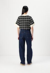 Knit black and white check-patterned short-sleeve cropped top paired with high-waisted blue denim wide-leg jeans and beige footwear.