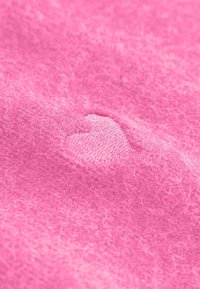 Różowa dziana tkanina z haftem w kształcie serca, o miękkim, teksturowanym wyglądzie i jednolitym, jasnym kolorze.