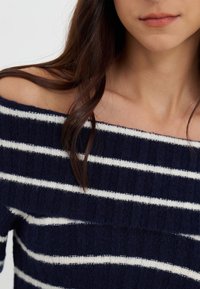 Marineblauwe trui met witte horizontale strepen, off-the-shoulder ontwerp, ribbeltextuur en een zachte gebreide stof.