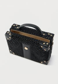 Čierna tkaná kabelka so štruktúrovaným tvarom, koženými akcentmi, zlatými cvočkami a horným uchom; vyznačuje sa elegantným, minimalistickým dizajnom.