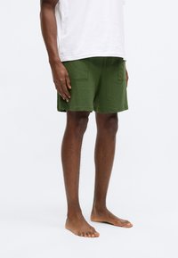 Πράσινο σορτς από απαλό ύφασμα, με άνετη εφαρμογή και δύο πίσω τσέπες, συνδυασμένο με μια απλή λευκή μπλούζα.