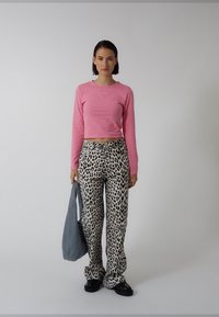 Roze cropped top met lange mouwen gecombineerd met losse broek met luipaardprint, en een grijze shopper in de hand. Glad stof, casual pasvorm en opvallend patroon.