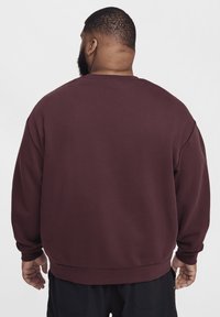 Sweatshirt vinho com um corte solto e mangas compridas. Apresenta punhos e barra canelados, textura suave e um design de gola redonda.