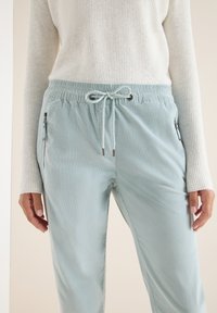 Pantaloni azzurri chiari con vita elastica, cordoncino e tasche laterali con zip. Realizzati in un tessuto morbido e strutturato, progettati per il massimo comfort.
