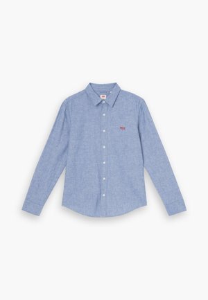 Hellblaues Hemd mit langen Ärmeln, Kragen und einem kleinen roten Logo auf der Brust. Der Stoff hat eine weiche, strukturierte Oberfläche.