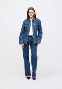 Τζιν μπουφάν με ελαφρώς φαρδιά εφαρμογή, δύο τσέπες στο στήθος και κλείσιμο με κουμπιά. Συνδυάζεται με ψηλόμεσα τζιν καμπάνα, όλα από μπλε τζιν ύφασμα.