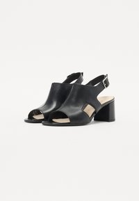 Sandales à talons ouverts en cuir noir avec un talon carré et une bride à la cheville ajustable. Texture lisse avec un design minimaliste.