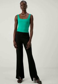 Fitted, sleeveless green top paired with black flared trousers. Smooth fabric, minimal detailing, and open-toed black sandals.