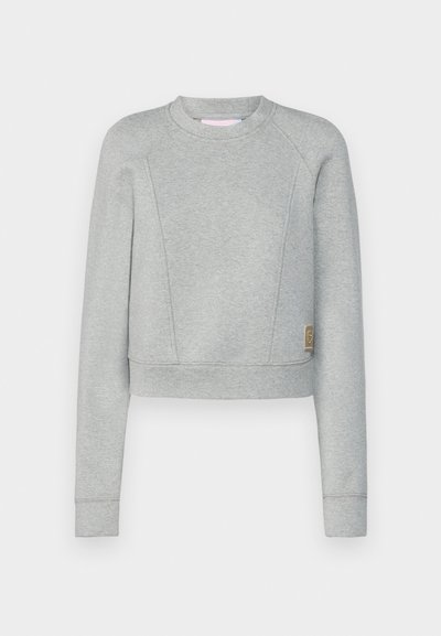 Sudadera gris recortada con mangas largas, hecha de un tejido suave. Presenta un cuello redondo, mangas raglán y un pequeño parche con logo en el costado.