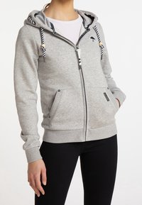 Sudadera con cremallera de color gris, hecha de una suave mezcla de algodón. Presenta una capucha con cordones, acentos a rayas y bolsillos frontales con cierres a presión.