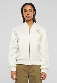 Off-white bomberjakke med glidelås, ribbestrikkede mansjetter og brodert logo på brystet. Gla glatt tekstur, skreddersydd passform og sidelommer.