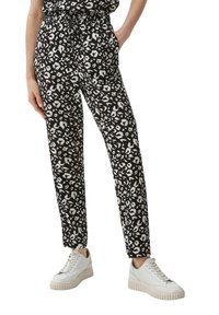 Un pantalon à motifs noir et blanc avec une taille à cordon de serrage et des poches latérales, associé à des baskets blanches avec une semelle texturée.