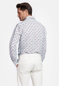 Heren overhemd met lange mouwen in lichtblauw met een bloemenpatroon in bruin en marineblauw. Voorzien van een klassieke kraag en een knoopsluiting aan de achterkant.