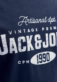 Camiseta de algodón azul marino con gran texto en blanco. El diseño incluye "Artisanal dpt. VINTAGE PREMIUM JACK & JONES CPH 1990" con un efecto texturizado.