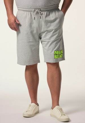 Man draagt lichtgrijze trekkoordshorts met "MIAMI BEACH" in groene tekst op het linkerbeen en witte sneakers, staand met handen in de zakken.