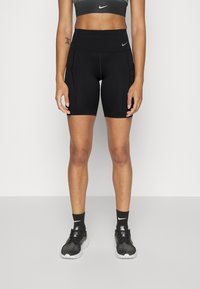 Pantalones cortos deportivos negros con una cintura alta, que cuentan con bolsillos laterales y una textura suave. Combinados con un sujetador deportivo negro a juego y zapatillas.