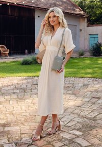 Cream wrap dress with short sleeves and textured fabric, paired with pale pink block-heeled sandals and a light green crossbody bag.